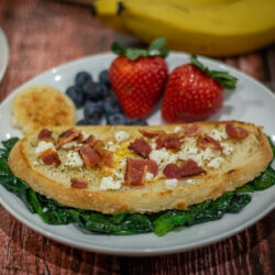 Bird in a Nest on a plate with sautéed spinach, strawberries, and blueberries.