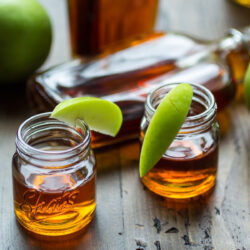 Caramel apple bourbon served in Mason jars, garnished with apple slices.