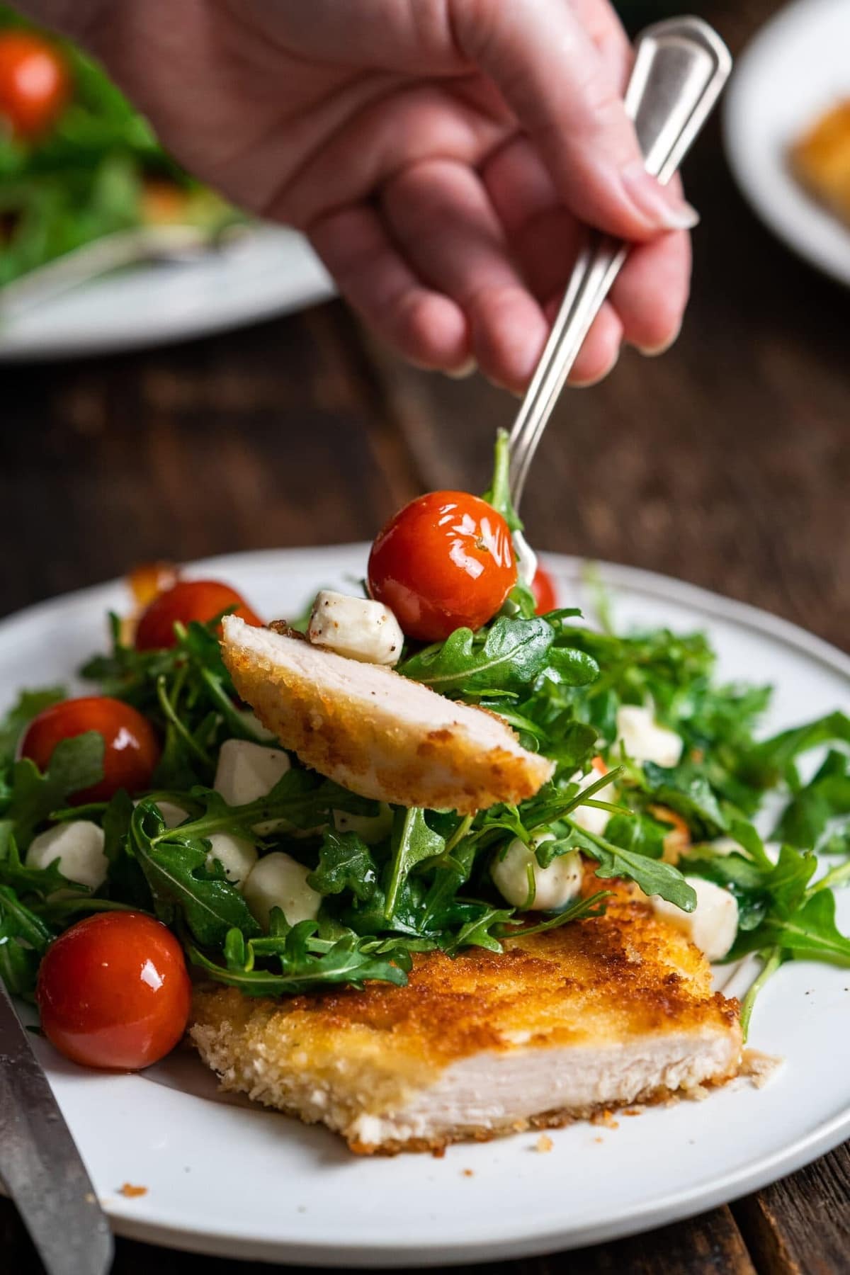 Chicken Paillard on a white plate topped with arugula and mozzarella balls.