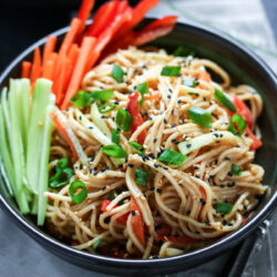 A bowl of cold sesame noodles, garnished with black and white sesame seeds.