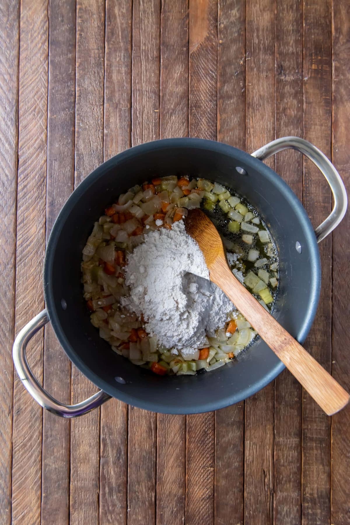 Adding flour in the pot with vegetables to make a roux.