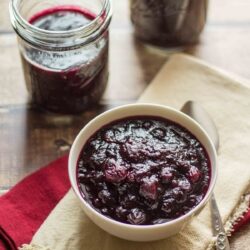 Cranberry sauce in a bowl and a Mason jar with cranberry sauce on a table.