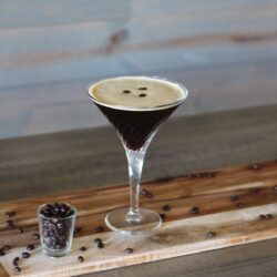 A glass of Espresso Martini and a shot glass filled with coffee beans.