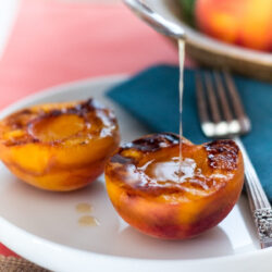 Grilled peaches being drizzled with honey on a white plate.