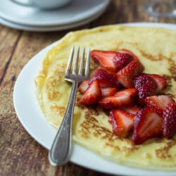 A plate of Swedish pancakes topped with fresh strawberries.