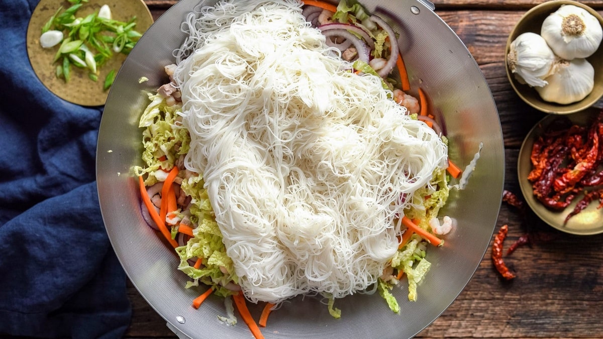 Hydrated noodles added in a wok with vegetables.