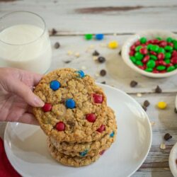 Monster Cookies stacked on a white plate with a glass of milk in the background.