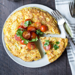 Potato Chip Spanish Tortilla topped with halved tomatoes and parsley.