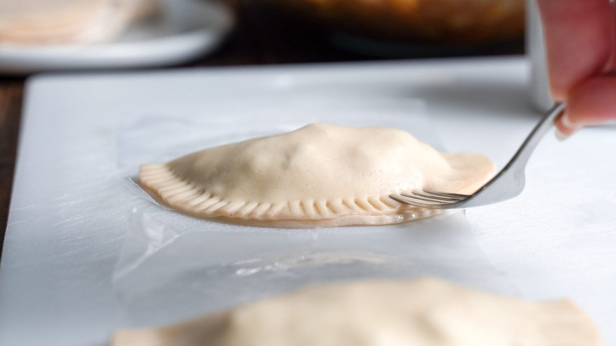 Empanada being sealed with a fork.