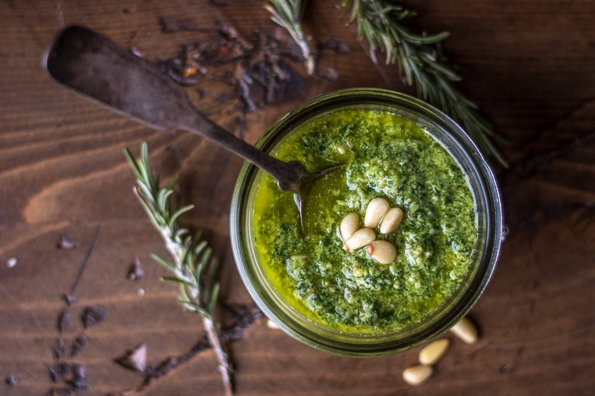 A jar of Arugula Pesto with Rosemary, garnished with pine nuts.