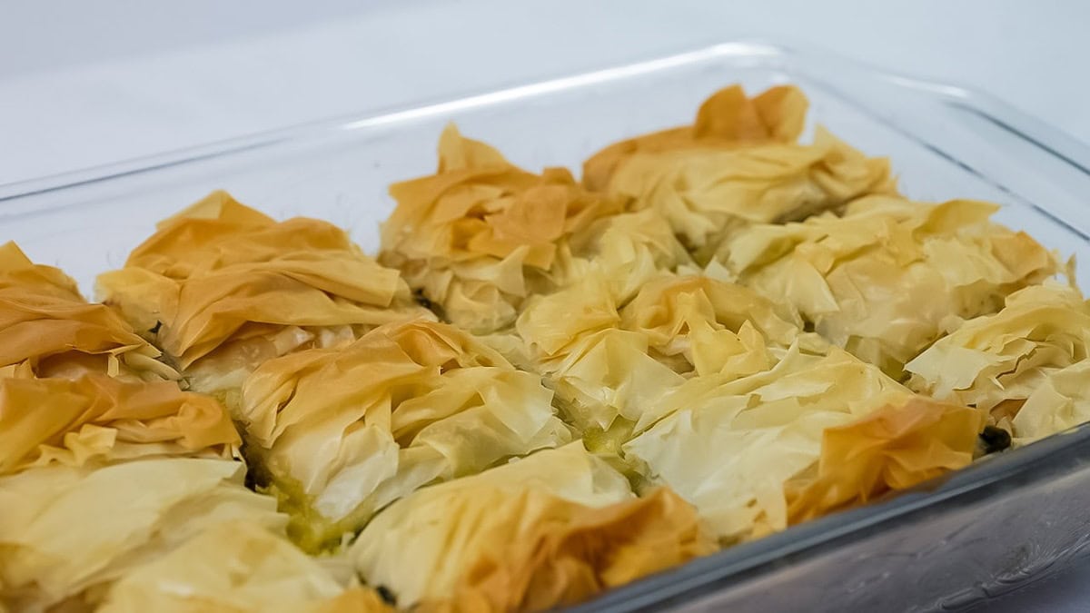 Baked Spanakopita cut into squares on a baking dish.